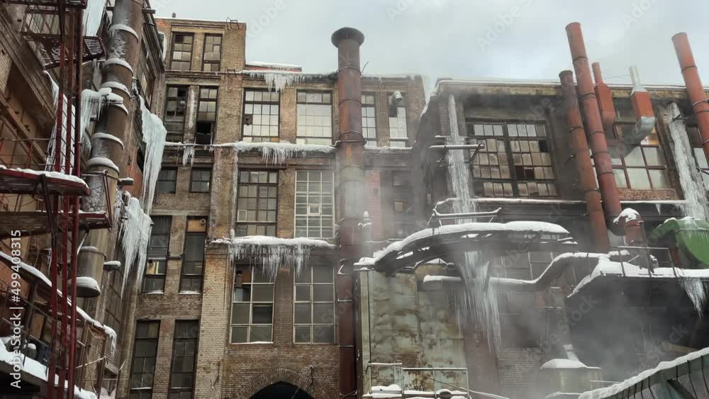 Facade of a former abandoned old factory dirty and covered in icicles in winter in frost