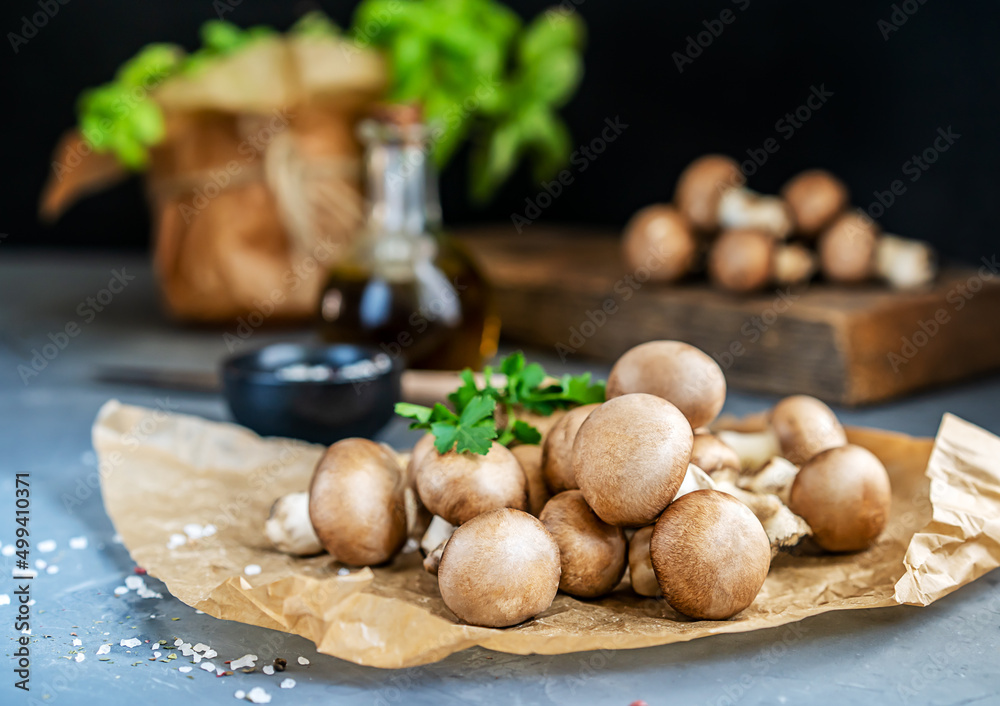 Group of raw creamy mushrooms champignons, olive oil, spices and basil plant on grey background. 