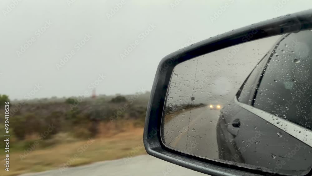Side mirror view driving on a grey rainy day