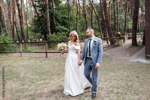 Smiling wedding couple in love in the forest hold hands and hug. Sunny day, good mood. Blonde girl © Denys