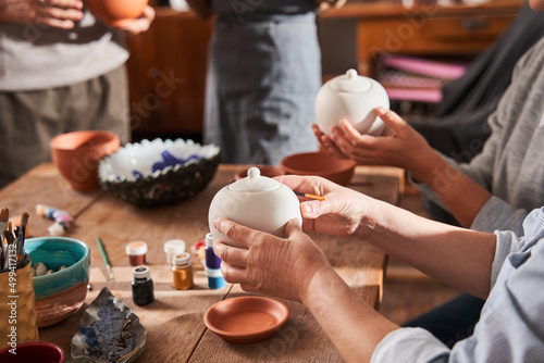 Mature ladies holding clay teapots and preparing to glaze it at their own taste