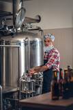 Shot of senior with gray hairs around huge barrel in brewery with modern equipment.