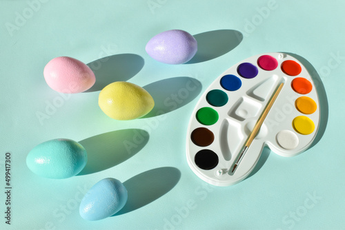 Paints and Easter painted eggs on a light blue background. Flat position, top view