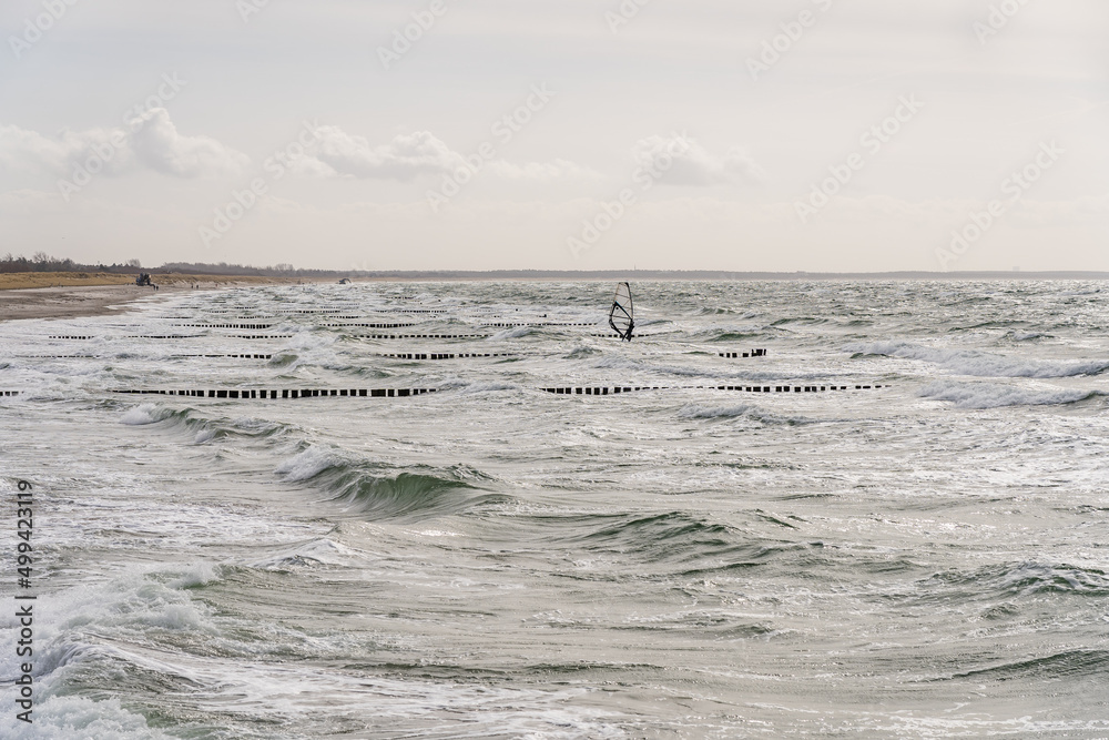 Lonely windsurfer in the ocean waves and groynes in between on a sunny afternoon Lonely windsurfer in the ocean waves and groynes in between on a sunny afternoon