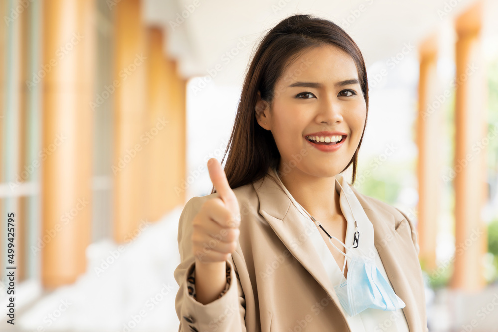 Happy office worker giving thumb up with no face mask on in post pandemic world, but still having precautionary face mask Happy office worker giving thumb up with no face mask on in post pandemic world, but still having precautionary face mask