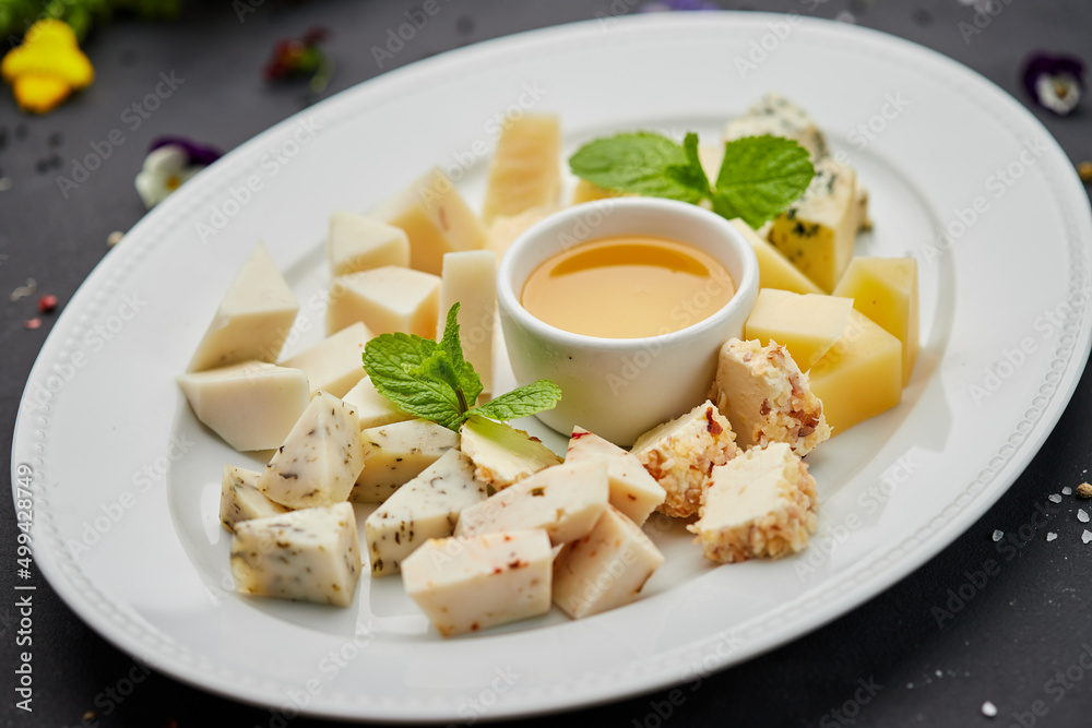 Cheese plate: Parmesan, cheddar, gouda, mozzarella and other with honey on white plate on dark background . Tasty appetizers. Top view. Photo for restaurant menu