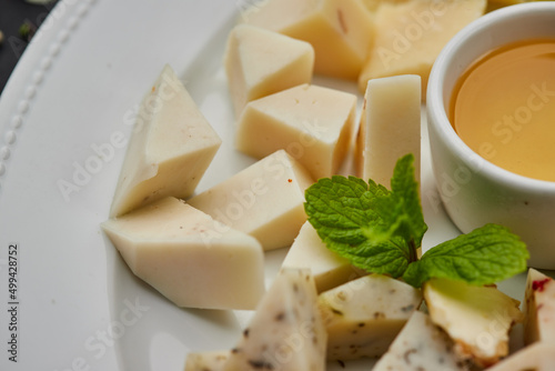 Cheese plate: Parmesan, cheddar, gouda, mozzarella and other with honey on white plate on dark background . Tasty appetizers. Top view. Photo for restaurant menu