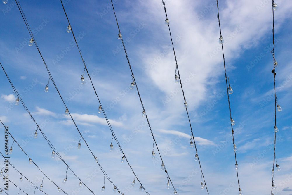 Fototapeta premium Wires with light bulbs on wires against cloudy blue sky background