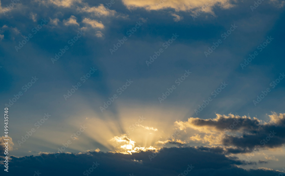 Sun rays streaking upwards from clouds against sky Sun rays streaking upwards from clouds against sky