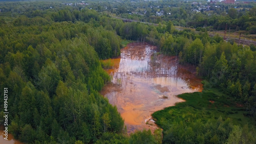 Polluted river. Clip. A dirty red river with a beautiful forest around and behind the houses.