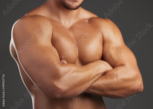 Confidently macho. Closeup shot of an unrecognizable and athletic young mans chest while he poses arms folded in studio against a dark background.