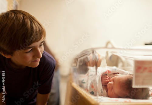 Boy (12-13) looking at newborn baby sister (0-1 months) in incubator photo