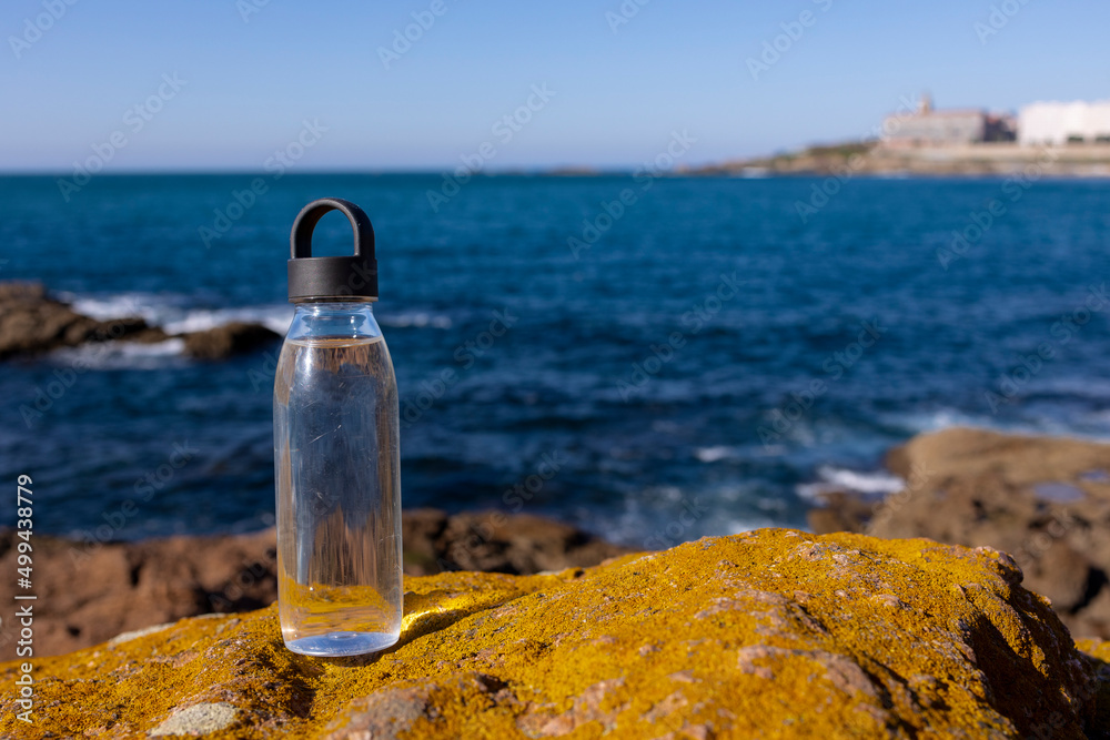 A bottle of water stands on a stone against the background of the ocean. A bottle of water stands on a stone against the background of the ocean.