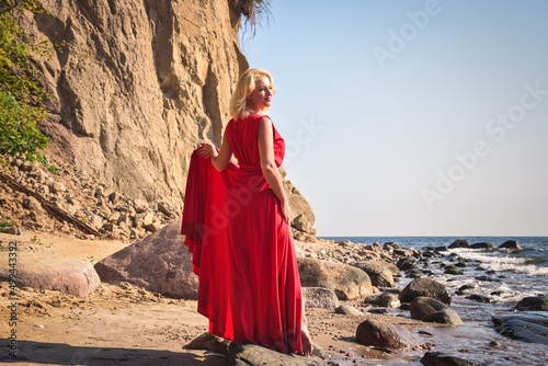 Creative holiday seaside session. Beautiful woman on the seashore in an elegant red dress.