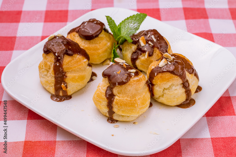 Profiteroles with chocolate sauce on white plate side view Profiteroles with chocolate sauce on white plate side view