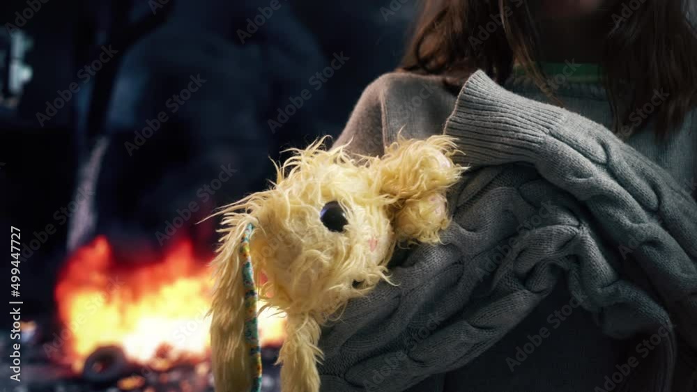 A little girl with her favorite plush toy in her hands against the background of a burning destroyed house. War and children, war crimes, terrorism, no war. A little girl with her favorite plush toy in her hands against the background of a burning destroyed house. War and children, war crimes, terrorism, no war.
