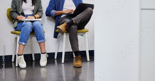 Were all trying to find our place in life. Shot of two unrecognizable people using their devices while waiting to be interviewed in a modern office.