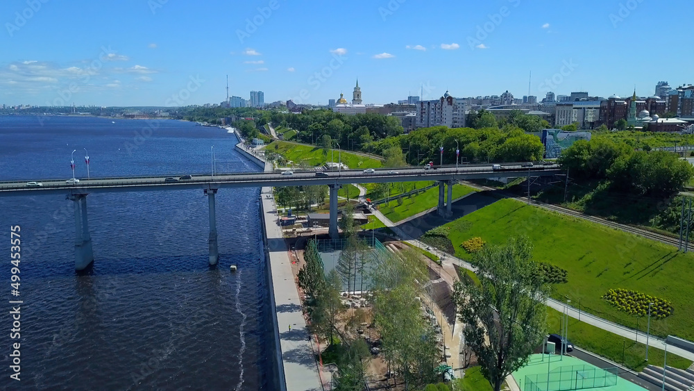 The view from the drone. Clip. A huge bridge crossing the river with cars next to the park and large houses.