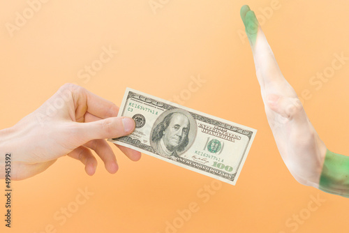 Say no dollar. The hand gesture of Nigeria rejects dollars. An arm holds 100 dollars, the other arm painted in the Nigerian flag doesn't want to take it. Isolated on yellow background. Wrong. Paying photo