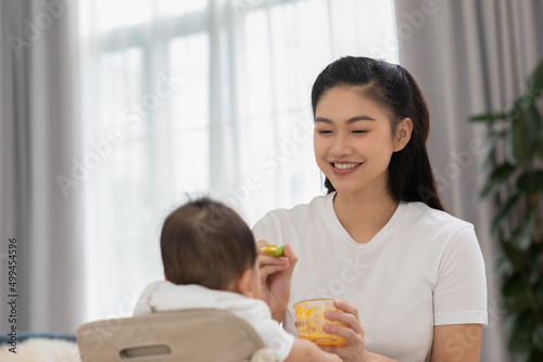 Mother feeding her asian baby daughter with pumpkin mashed or vegetable mash for vitamin on rubber spoon.Mom trying feed little baby boy at home enjoy and spending time together.Baby feeding Concept
