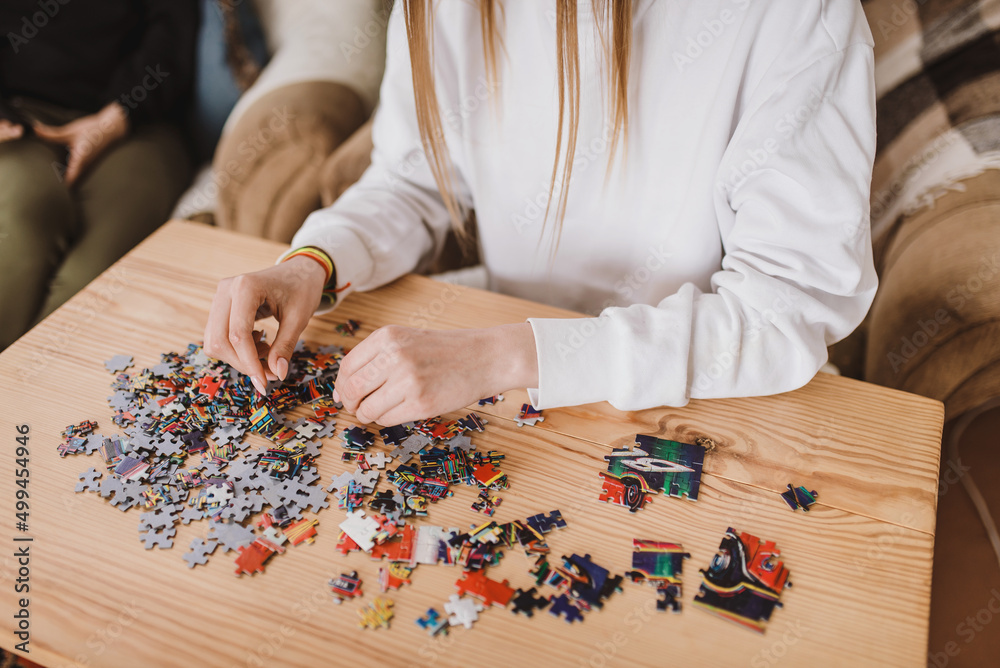 Young woman doing jigsaw puzzles close up. Hands and pieces of puzzles picture laying in pile on the wooden table Young woman doing jigsaw puzzles close up. Hands and pieces of puzzles picture laying in pile on the wooden table