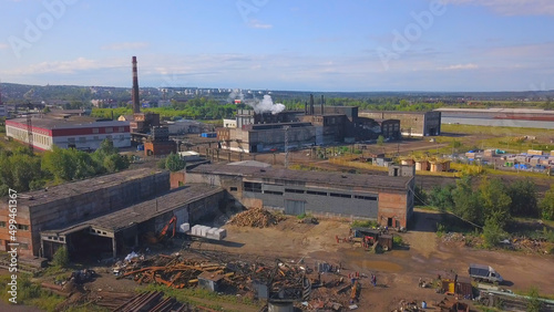 View of the work area from the drone. Clip. A large factory with pipes from which smoke is coming, the city and the forest and the calm sky are visible from behind.