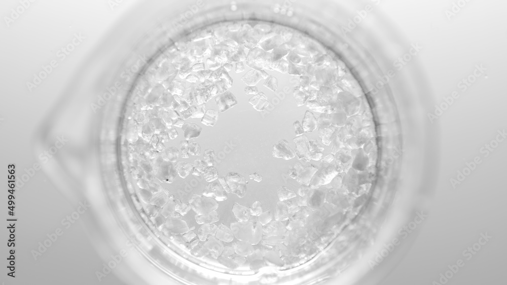 Top view macro shot of crystals dissolving in clear fluid in beaker on light grey background | Mineral skincare cosmetics formulating concept Top view macro shot of crystals dissolving in clear fluid in beaker on light grey background | Mineral skincare cosmetics formulating concept