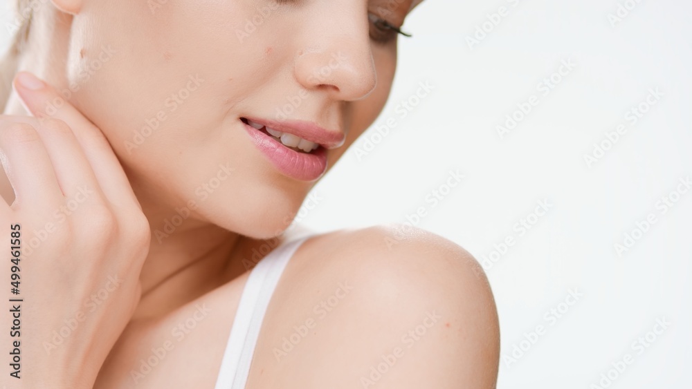 Big close-up shot of young Caucasian woman who touches her jaw line turning her head and looking aside on white background | Skin care commercial concept