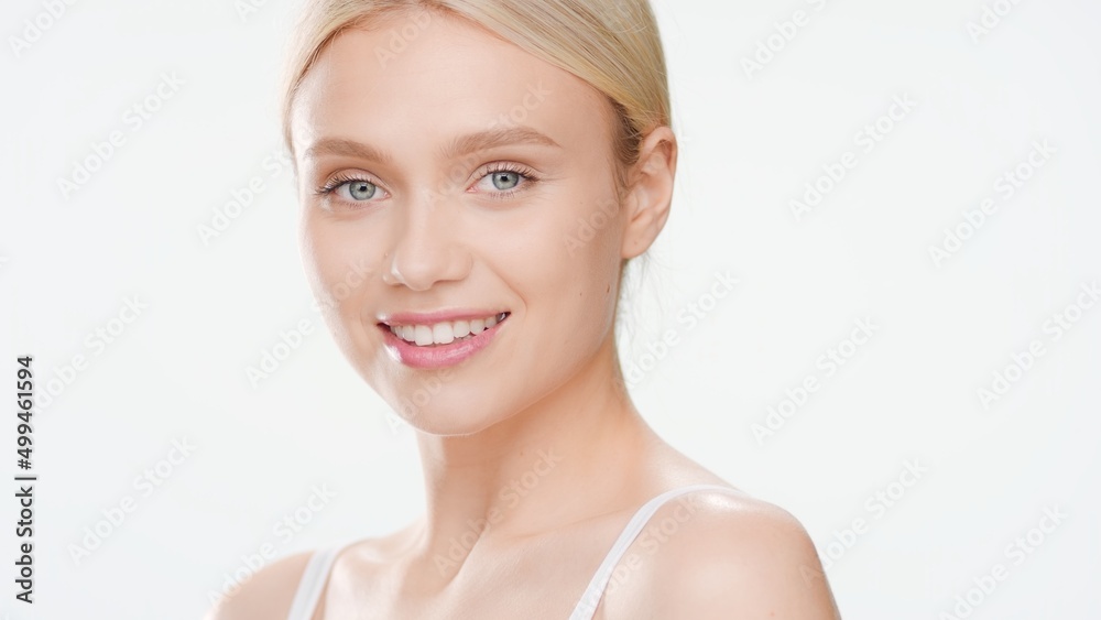 Young blond Caucasian woman half-turned to camera smiles on white background | Face skin care concept Young blond Caucasian woman half-turned to camera smiles on white background | Face skin care concept