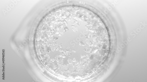 Top view macro shot of crystals dissolving in clear fluid in beaker on light grey background | Mineral skincare cosmetics formulating concept