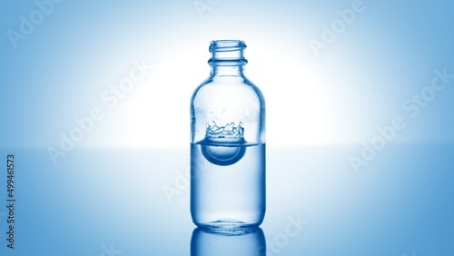 Drop of hypochlorous acid falls down into medical bottle with blue transparent liquid and makes crown splash inside it against blue background | Abstract cosmetics formulating concept