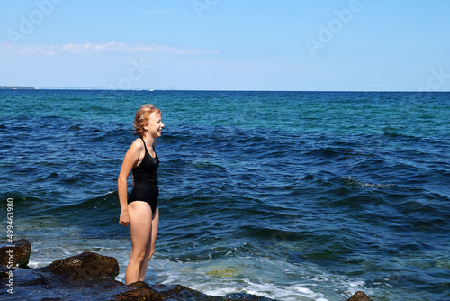 smiling teenage girl in a black swimsuit on the background of the sea horizon