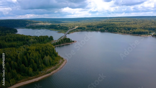 A huge bridge across the river. Clip. Bird's-eye view. A huge bridge over a large river against the background of a cloudless sky and huge forest trees.