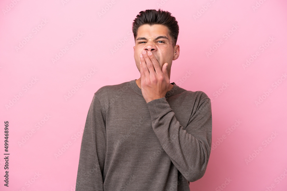 Young caucasian man isolated on pink background yawning and covering wide open mouth with hand