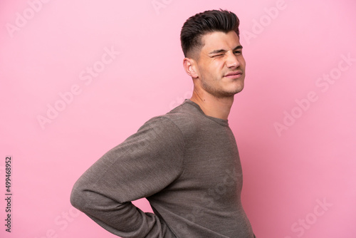 Young caucasian man isolated on pink background suffering from backache for having made an effort