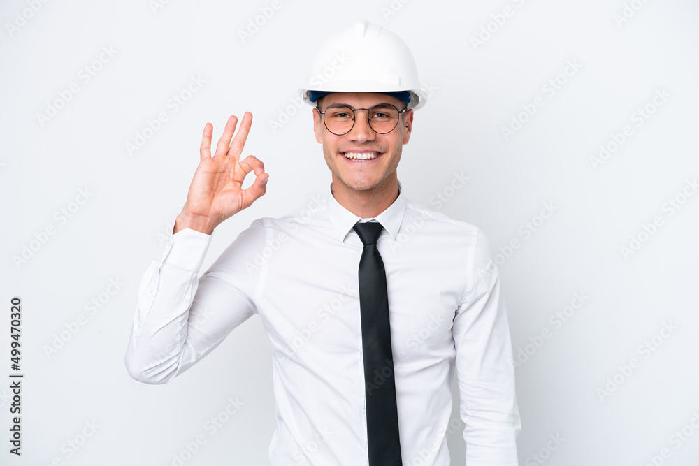Young architect caucasian man with helmet and holding blueprints isolated on white background showing ok sign with fingers Young architect caucasian man with helmet and holding blueprints isolated on white background showing ok sign with fingers