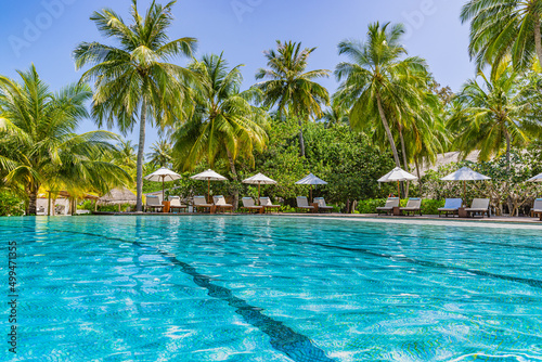 Beautiful luxury umbrella and chair with outdoor swimming pool in tropical beach hotel resort. Coconut palm trees at poolside. Summer travel vacation background concept. Amazing relax, freedom scenic