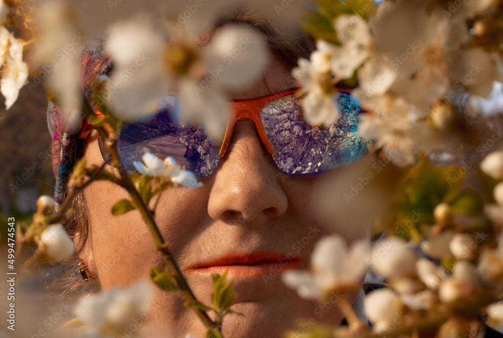 Spring composition. Face of a pretty adult woman in sun glasses framed by tree flowers Spring composition. Face of a pretty adult woman in sun glasses framed by tree flowers