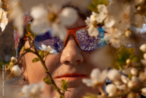 Fototapeta Naklejka Na Ścianę i Meble -  Spring composition. Face of a pretty adult woman in sun glasses framed by tree flowers
