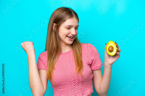Teenager Russian girl holding an avocado isolated on blue background celebrating a victory © luismolinero