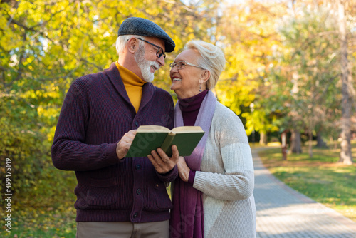 Senior couple walking in park and reading a book.