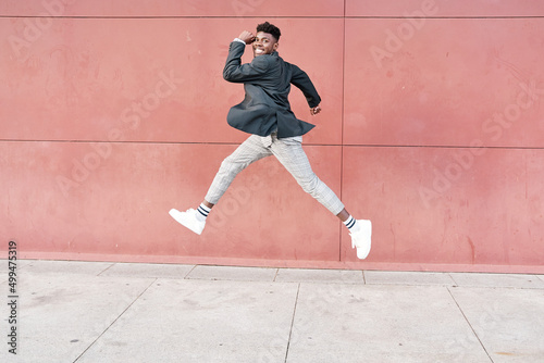 Full length portrait of a cheerful afro american man jumping isolated on a red background