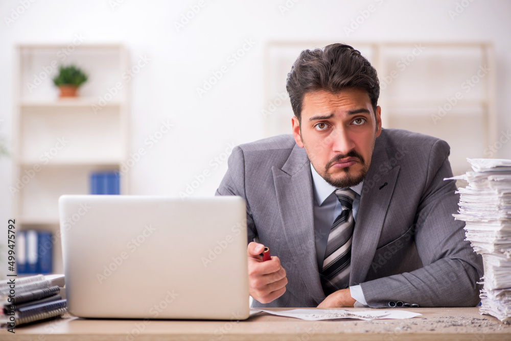 Young male employee unhappy with excessive work in the office Young male employee unhappy with excessive work in the office