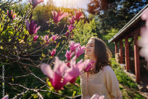 Obraz na płótnie Young beautiful woman enjoying the spring of her home in the garden near a blooming magnolia tree inhaling the aroma of flowers w salonie