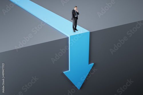 Attractive young european businessman standing on abstract blue arrow falling down cliff. Crisis and failure concept.