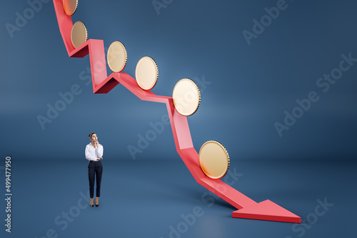 Attractive thoughtful young businesswoman with abstract falling red arrow with empty golden coins on blue background with mock up place. Crisis, downfall and currency concept. photo