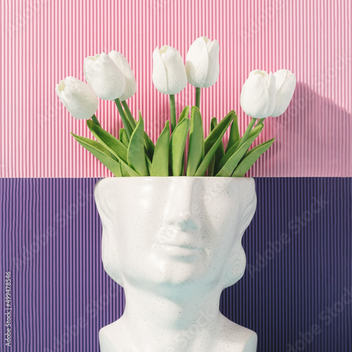 Stone head sculpture with tulip flowers on a pink and purple background. Spring, summer artistic concept. photo