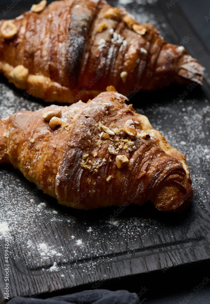baked croissants on a black wooden board sprinkled with powdered sugar