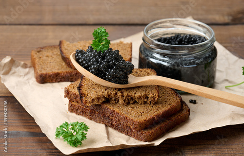 fresh grainy black paddlefish caviar in brown wooden spoon on a brown table, close up