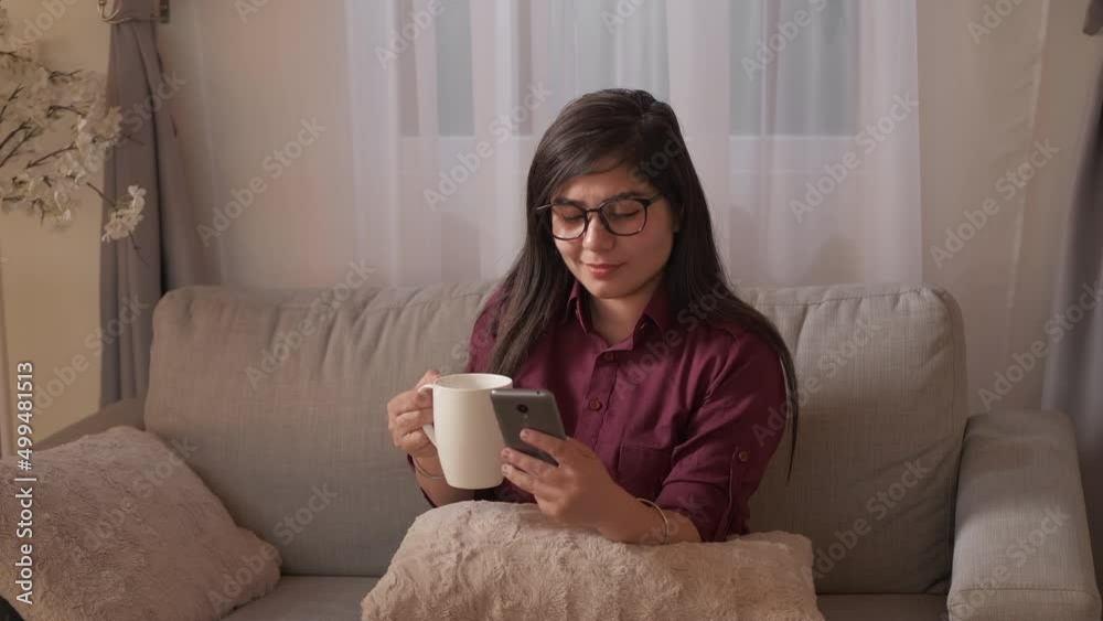 Coffee relax. Phone entertainment. Home leisure. Happy dreamy woman drinking cup of tea chatting on cell enjoying cozy weekend rest on couch at living room. Coffee relax. Phone entertainment. Home leisure. Happy dreamy woman drinking cup of tea chatting on cell enjoying cozy weekend rest on couch at living room.